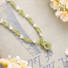 Introduce a touch of whimsy and elegance to your jewelry collection with the Pearl Avocado Necklace. This unique piece features a charming avocado pendant, exquisitely detailed with vibrant enamel to capture the fruit's natural beauty. The pendant is complemented by a delicate strand of lustrous pearl beads, adding a sophisticated touch to this playful design. Crafted from durable brass and plated in luxurious 18K gold, the gold avocado necklace ensures both quality and longevity. The avocado, a Green Pearl Pendant Jewelry Gift, Green Beaded Teardrop Pendant Jewelry, Green Pearl Pendant Jewelry As Gift, Charming Pearl Charm Jewelry For Gift, Green Beaded Charm Necklaces As Gift, Pear-shaped May Birthstone Necklace Gift, Green Dainty Necklace With Charms, Green Pear Shaped Necklace Gift, Green Dainty Necklaces With Charms