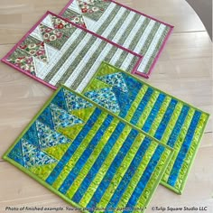 three quilted placemats sitting on top of a wooden table next to each other