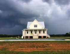 a large white house sitting on top of a lush green field under a cloudy sky