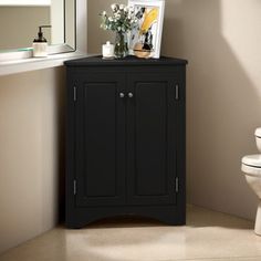 a black cabinet next to a toilet in a bathroom with a mirror on the wall