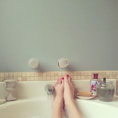 a person's feet in a bathtub with soap and other items on the counter