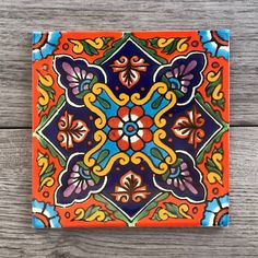 an orange, blue and yellow tile with flowers on the bottom is sitting on a wooden surface