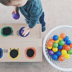 a toddler playing with colored balls in a cardboard box