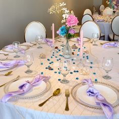 the table is set with white plates and purple napkins, silverware, and pink flowers