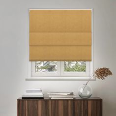 an orange roman blind in a white room next to a wooden cabinet with books on it