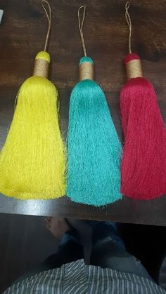 three different colored tassels hanging from a wooden shelf with string attached to them