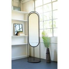 a tall mirror sitting on top of a metal stand next to a vase with a plant in it