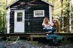 a woman and her dog sitting on the porch of a tiny cabin in the woods