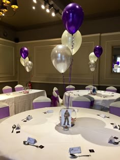 the table is set up with purple and white balloons, place cards, and silver confetti