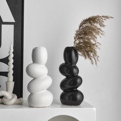 three black and white vases sitting on top of a shelf next to a plant