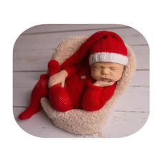 a newborn baby wearing a santa hat and sleeping in a red knitted blanket on a white wooden floor