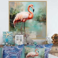 a pink flamingo standing on top of a blue pillow next to a painting and other items