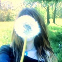 a woman holding a large dandelion in her hand and blowing it into the air