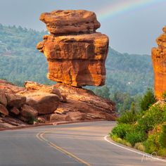 a rainbow shines in the sky over a road with large rocks on both sides