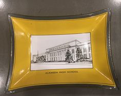 a yellow and silver tray with a drawing of a building on the front in black ink