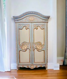 an ornate armoire in the corner of a room with wood floors and white walls