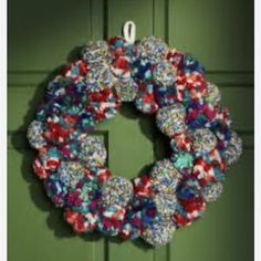 a wreath hanging on the front door of a green house with red, white and blue flowers