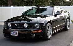 a black mustang parked in front of a white fence