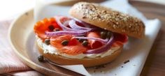 a bagel sandwich with salmon, onions and capers on a wooden platter