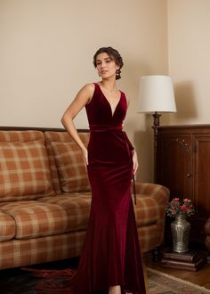 a woman standing in front of a couch wearing a red velvet dress with deep v - neck