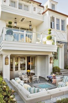 an outdoor patio with white furniture and potted plants on the side of the house