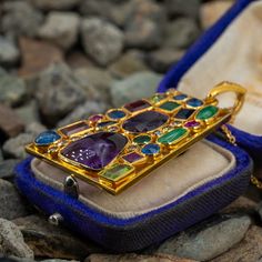 This gorgeous 18K yellow gold enhancer pendant is bezel set with six (6) natural blue sapphires, two (2) natural peridot, two (2) natural emeralds, two (2) natural jadeite jade, two (2) natural pink sapphires, two (2) natural purple sapphires, two (2) natural amethyst and eleven (11) round brilliant cut diamonds. The tapered bail is bead set with two (2) round brilliant cut diamonds. The pendant measures 48.00mm X 31.00mm and is suspended from a 14K yellow gold neck chain measuring 18 inches in length. One of the peridots is lightly chipped. Gold Rectangular Multi-stone Jewelry, Fine Jewelry Cabochon Gemstone Pendant, Antique Multi-stone Pendant Jewelry, Gold Gemstones Jewels Gift, Gold Gemstones For Gifts, Multi-stone Pendant Gemstones For Jewelry Making, Gold Neck Chain, Purple Sapphire, Neck Chain