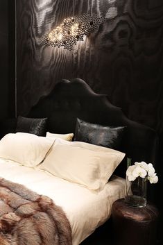 a bed with white sheets and pillows in a black walled room next to a night stand