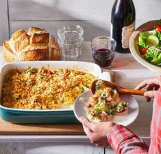 a person holding a plate with food in front of a casserole dish on a table