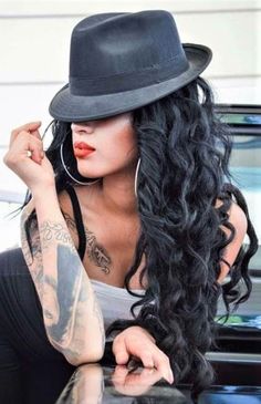 a woman with long black hair wearing a hat and sitting in front of a car