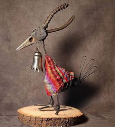 a metal bird sculpture on top of a wooden stump with a bell in it's beak