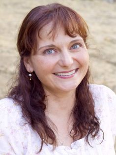 a woman with long red hair and blue eyes smiles at the camera while sitting on a beach