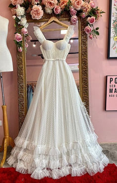 a white wedding dress on display in front of a mirror with pink flowers hanging from it