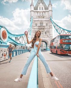 a woman standing on the edge of a bridge in front of a red double decker bus