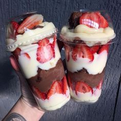 two desserts in plastic cups with strawberries and chocolate on top, sitting next to each other