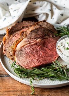 a white plate topped with meat and vegetables next to a bowl of ranch dressing on top of a wooden table