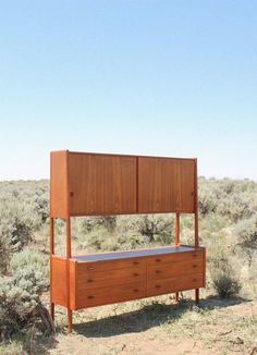 a wooden bed sitting on top of a dry grass covered field next to a bush