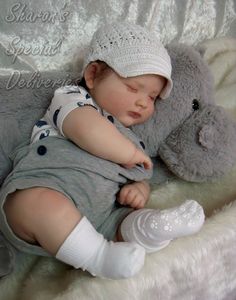 a baby laying on top of a white blanket next to a gray teddy bear wearing a hat