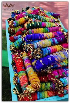 colorful bracelets are stacked on top of each other in a blue box with gold accents