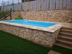 a small swimming pool with steps leading up to it and a stone wall around it