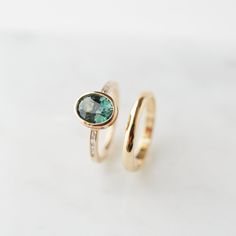 two gold rings with green and blue stones on them, one has a diamond in the middle