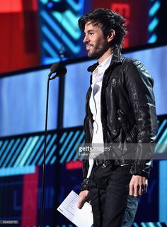 a man standing in front of a microphone on top of a stage holding a piece of paper