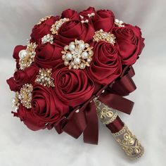 a bridal bouquet with red roses, pearls and brooches is on display