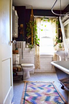 a bath room with a toilet a tub and a rug on the floor in front of a window