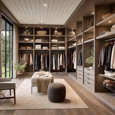 a large walk in closet with lots of clothes on hangers and drawers, along with a footstool