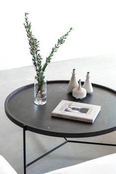 a black table with two vases and a book on the top, sitting in front of a white chair