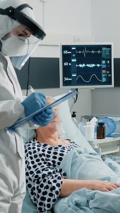 a person in a hospital bed with an oxygen mask on and another person wearing a protective suit