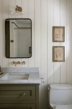 a white toilet sitting next to a bathroom sink under a mirror above a wooden vanity