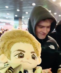 a man in a hoodie looking at a stuffed doll