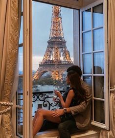 a woman sitting on a window sill looking out at the eiffel tower