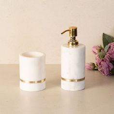 two white marble soap dispensers with gold trim and flowers in the background